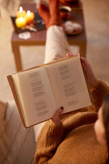 halloween, holidays and leisure concept - close up of young woman reading book and resting her feet...