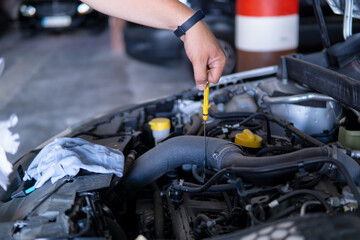 Auto mechanic working and removing the oil dipstick from the engine of a car in a garage.