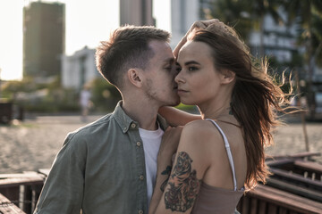 Lovely romantic couple smiling and kissing. Beautiful sunlights. Portrait. Millennial. Wearing...