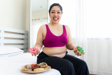 Obraz na płótnie Canvas Asian fat women , Fat girl , Chubby, overweight holding Junk food Sweet treat cake donut reason why you are fat in the bedroom - Woman lifestyle overweight problem concept
