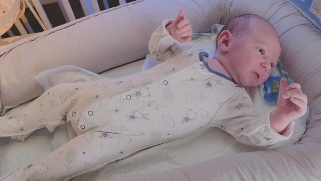 A newborn baby, one month old, rests restlessly in the crib, jerking his arms and legs