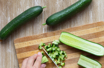 Top view of woman hand cutting fresh cucumbers on the wooden cutting board