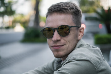 Naklejka na ściany i meble Close up portrait of young man in sunglasses wearing bright-green t-shirt and smiling. High quality photo