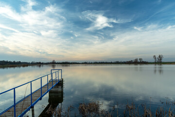 A narrow jetty on a calm lake and clouds