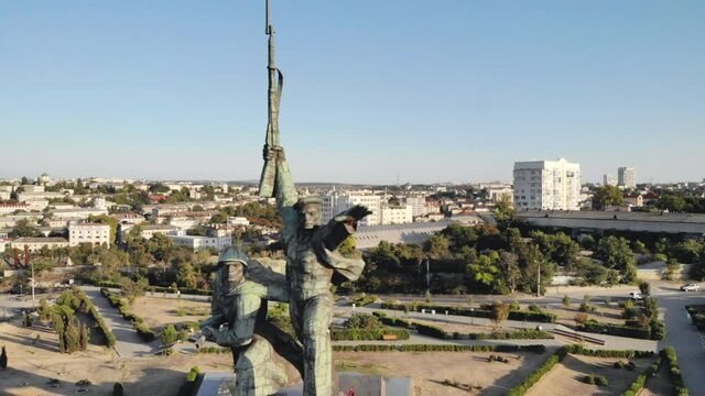 Aerial shot of soldiers monument on central city square. Drone flying above town park with beautiful cityscape at background. View to historic sculpture in urban area