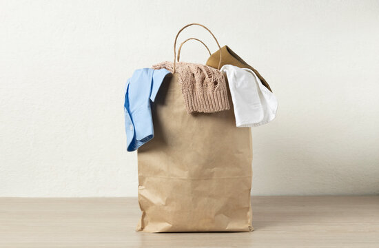 Paper bag full of used clothes for recycling on the desk against white wall.Empty space