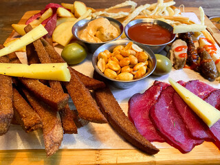 Beer platter with cold cuts, croutons, cheese, barbecue, beef, pork and chicken, potatoes, mustard sauce, ketchup and peanuts. Everything on a wooden platter.