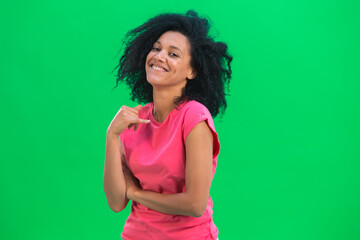 Portrait of young female African American flirtatious smiling. Black woman with curly hair in pink tshirt poses on green screen in the studio. Close up.
