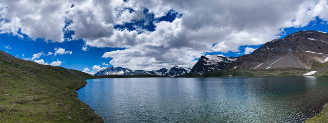 Scenic panoramic view of high mountains with clean lake and a blue sky with puffy clouds