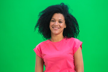 Portrait of young female African American smiling happily. Black woman with curly hair in pink tshirt poses on green screen in the studio. Close up.