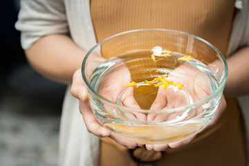 woman holding a clear cup of water There are yellow flowers inside.