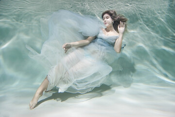 Girl underwater. model in water in a beautiful dress swims like a fish.In a blue flying dress. 