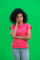 Portrait of young female African American suffering from headache from fatigue. Black woman with curly hair in pink tshirt poses on green screen in the studio. Close up.