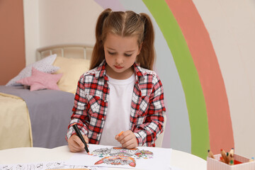 Little girl coloring antistress page at table indoors