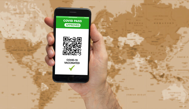 man hand holding a smart phone with a digital illustration of a Covid-19 health passport concept on blurred world map