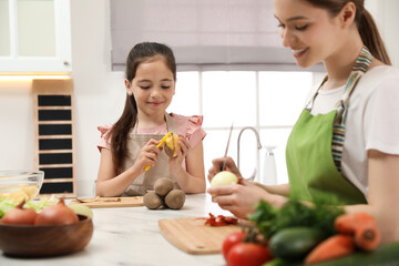 Mother and daughter peeling vegetables at table in kitchen