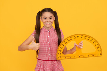 happy child hold school math tool protractor ruler on yellow background show thumb up, algebra