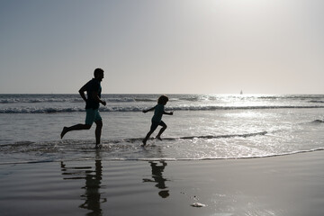 Fototapeta na wymiar father and son running on beach. daddy with kid boy in sea or ocean. weekend family day.