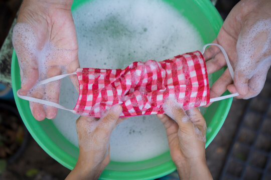 Mom And Kids Hand Washing A Mask Using Detergent Dissolved In Water. Washing The Masks Is Disinfecting And Saving Money To Be Used Again.