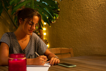 Caucasian teen girl thinking, smiling and writing in her notebook.