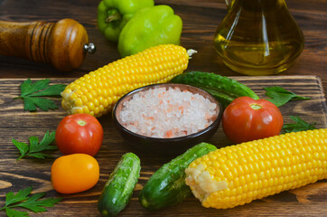 food background and ingredients for cooking summer salad, pink salt mineral, tomato, cucumber, mill pepper, corn, fresh vegetable on wooden table, vitamin for eating