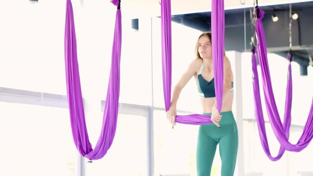 Young beautiful woman practice in stretching swing. Aerial flying yoga exercises practice in purple hammock in fitness club.