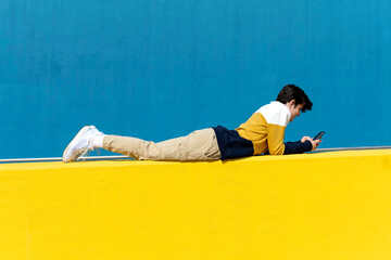 Young man using a smart phone texting messages , leaning on wall
