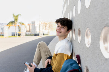 Happy young teen male sitting on urban bench while looking to camera
