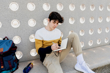 Young male writing notes in a notebook sitting on a bench