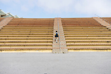 Rear view of a young student with backpack going up stairs of bleacher