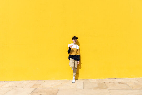 Young male on yellow background showing horn gesture