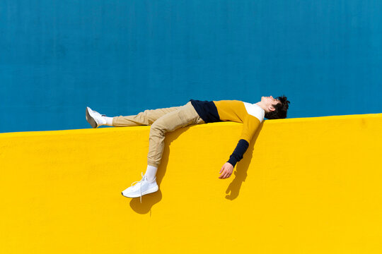 Young man relaxing on yellow wall against blue wall