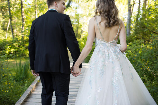 Rear view of well-dressed couple holding hands outdoors.