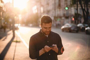 Happy man using smart phone standing on street in city in summer