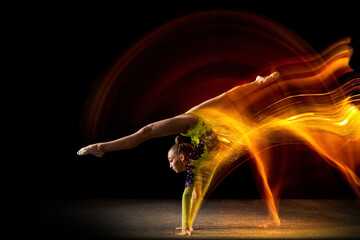 Portrait of young girl, rhythmic gymnastics artist in action isolated on dark studio background...