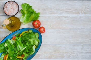 fresh summer green salad with vegetables cucumber, tomato, bell pepper, pink salt and leaf lettuce in ceramic bowl, dieting and vegan food on wooden background with copy space text