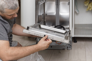 a man fixing a broken dishwasher at home