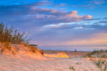 Sand dune illuminated by the setting sun and the shore of the Baltic Sea.