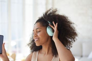 Young trendy woman in big headphones listening music and dancing at home. Enjoying audio streaming app on smartphone, leisure and relax at home alone