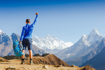 Hiker cheering elated and blissful with arms raised in the sky after hiking. Everest mountain on...
