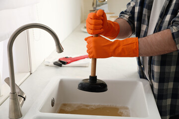Man using plunger to unclog sink drain in kitchen, closeup - obrazy, fototapety, plakaty