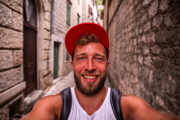 A smiling man with a red cap takes a selfie picture in the old town