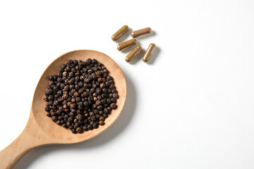 Black peppercorn in wooden spoon and capsule pills on white background.
