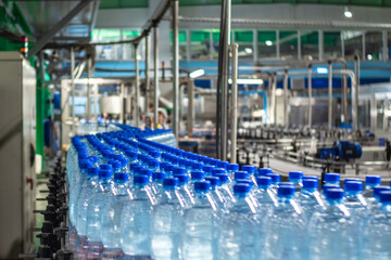 Blue plastic bottles in three rows with clean drinking water on a conveyor belt at a mineral water plant. Food production.