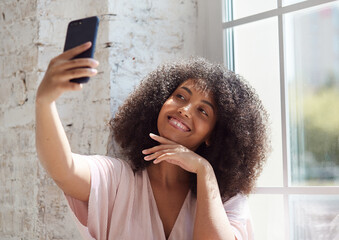 Female vlogger influencer sit at home speaking looking at camera, young african woman blogger greets fans and talks sitting near the window.