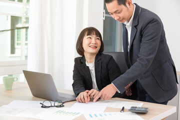Businesswoman and businessman working together with laptop and graphic charts while sitting at meeting table in modern office.