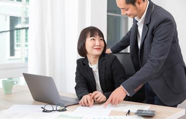 Businesswoman and businessman working together with laptop and graphic charts while sitting at meeting table in modern office.