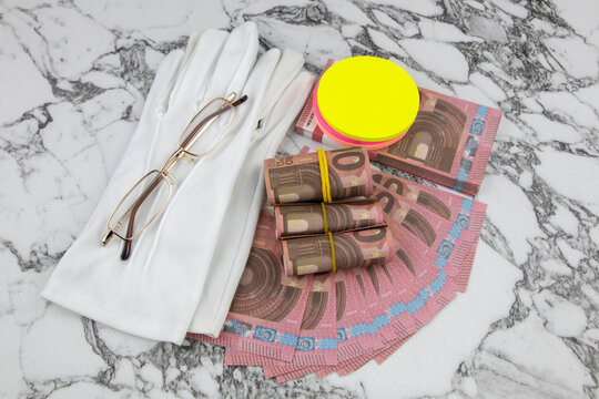 Financial or business concept with a pair of white gloves, eyeglasses and wads and fanned Euro banknotes with colorful circular memo pads over a white marble background in a flat lay view