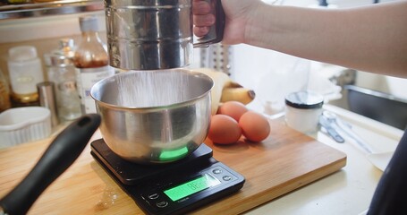 Hand of woman pastry chef sifting flour through sieve with a Sifter in the Kitchen with ingredients, preparing flour to baking cake bakery	
