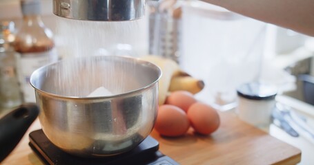 Hand of woman pastry chef sifting flour through sieve with a Sifter in the Kitchen with ingredients, preparing flour to baking cake bakery	

